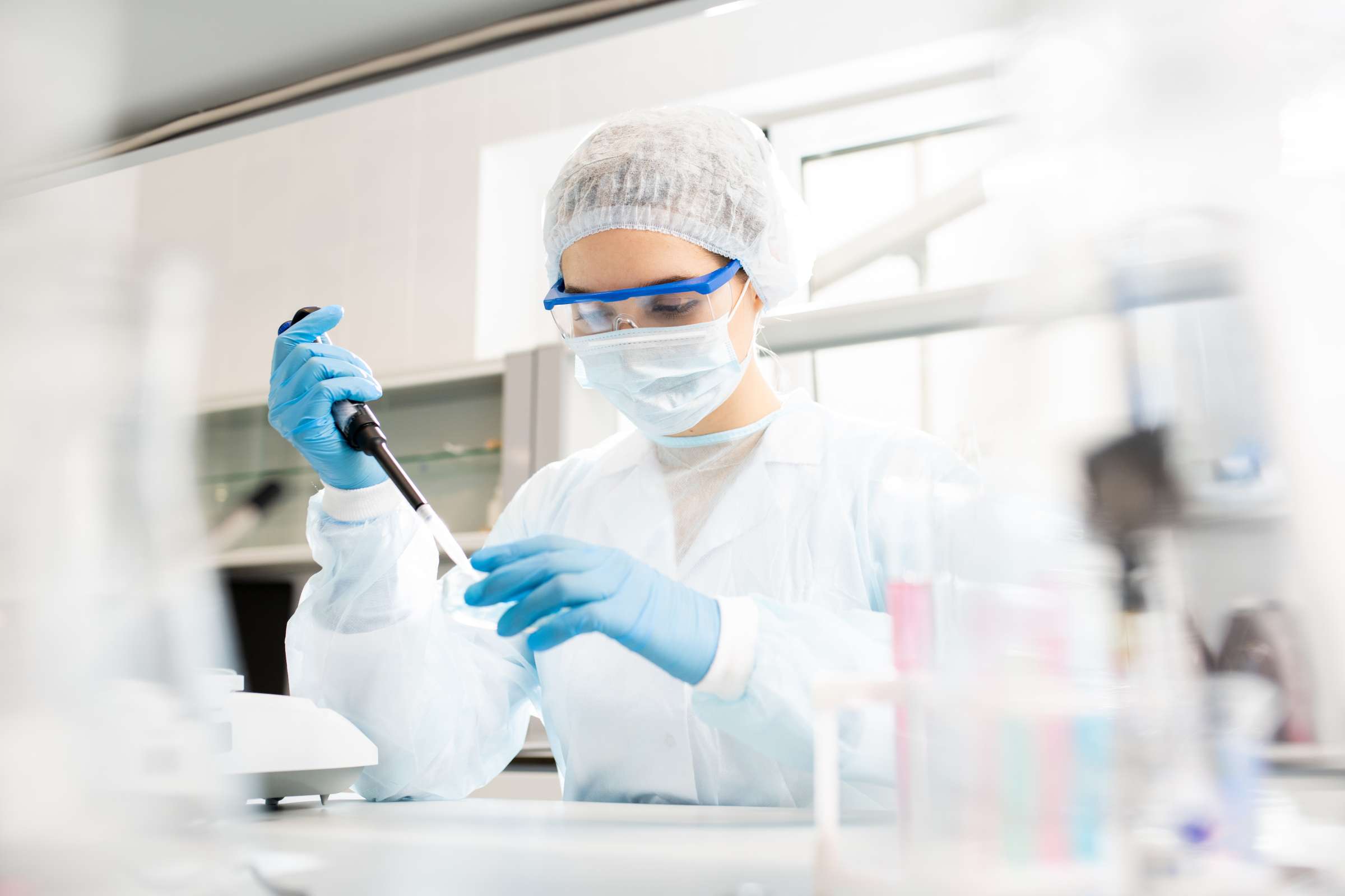 Researcher wearing personal protective equipment sits at a table while dropping reagent in a petri dish.
