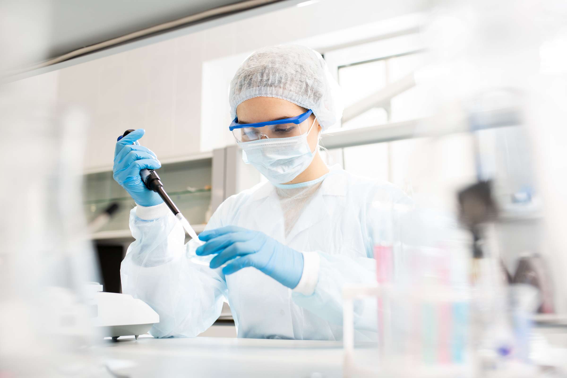 Researcher wearing  personal protective equipment sits at a table while dropping reagent in a petri dish.