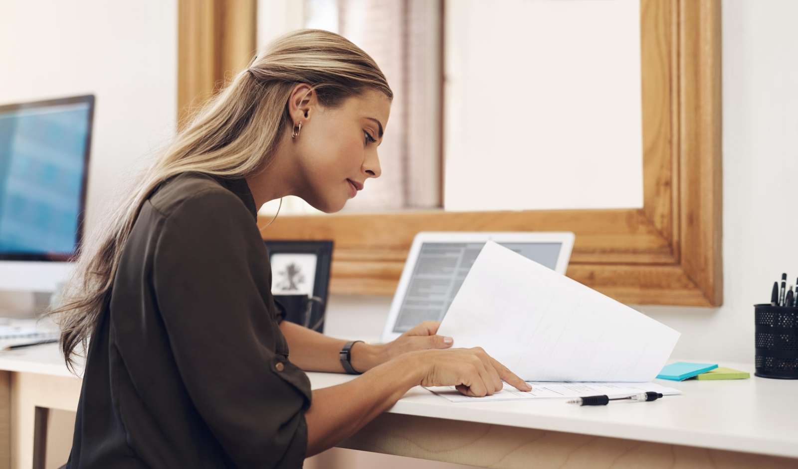 Employee sits at a desk in front of a laptop and points at a page in a document