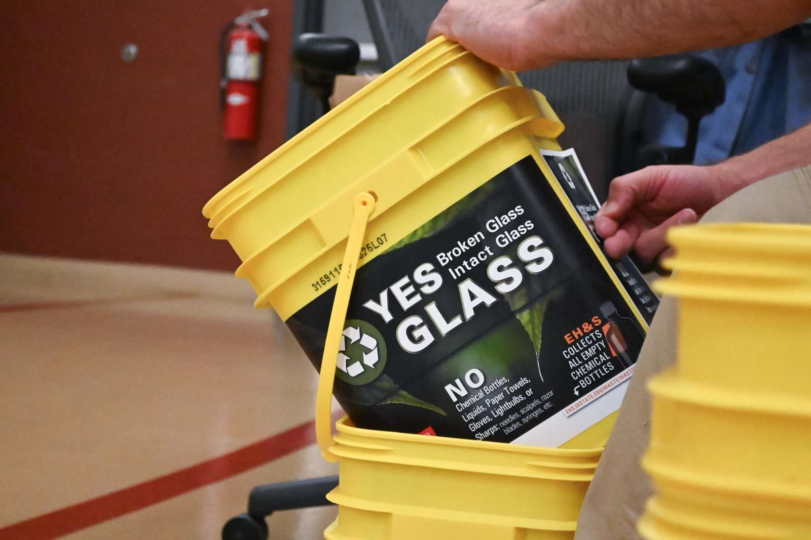 EH&S staff member places glass collection label on a donated Tidy Cats litter bucket.